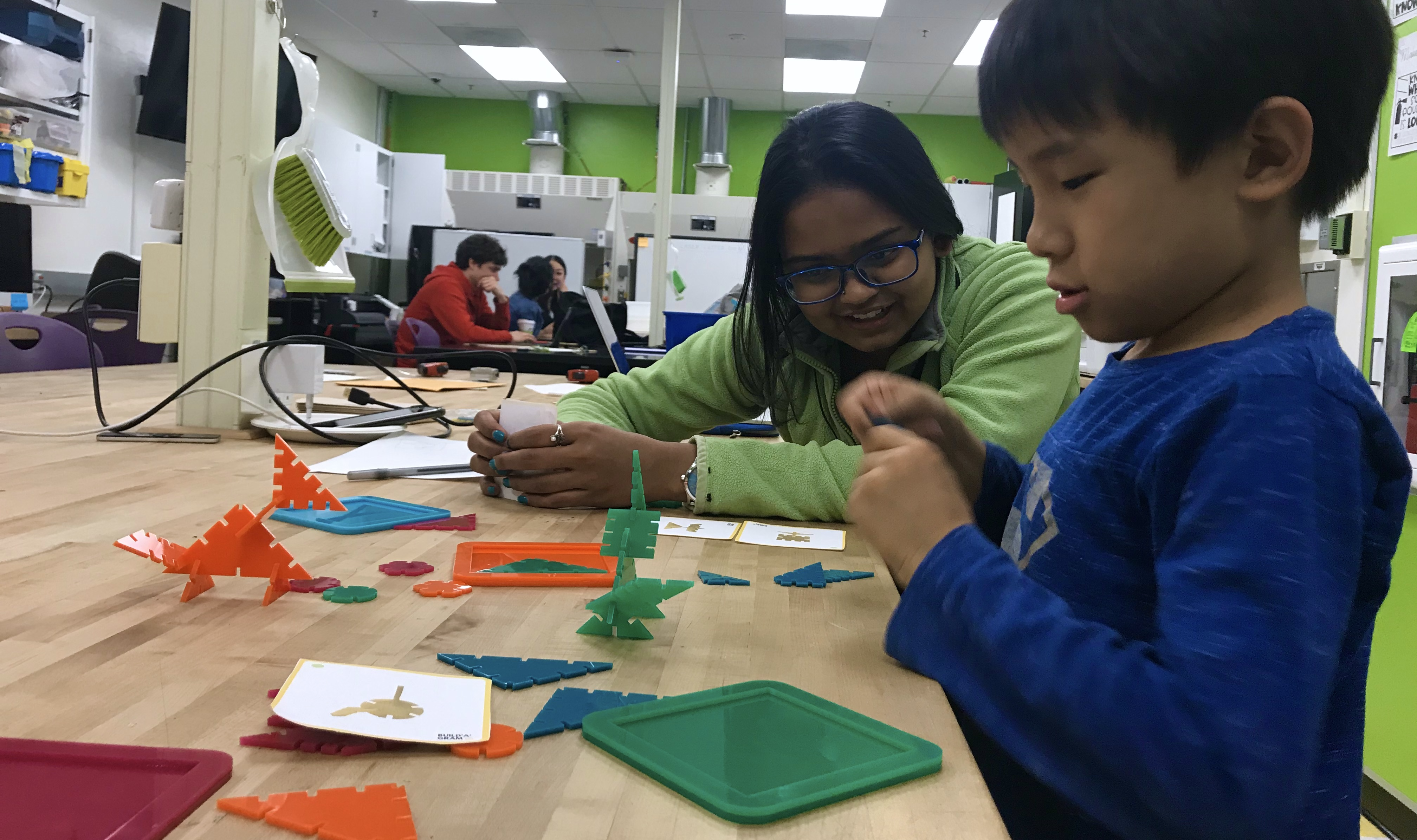 A young Asian boy and south Asian woman play-testing with colorful geometric pieces.