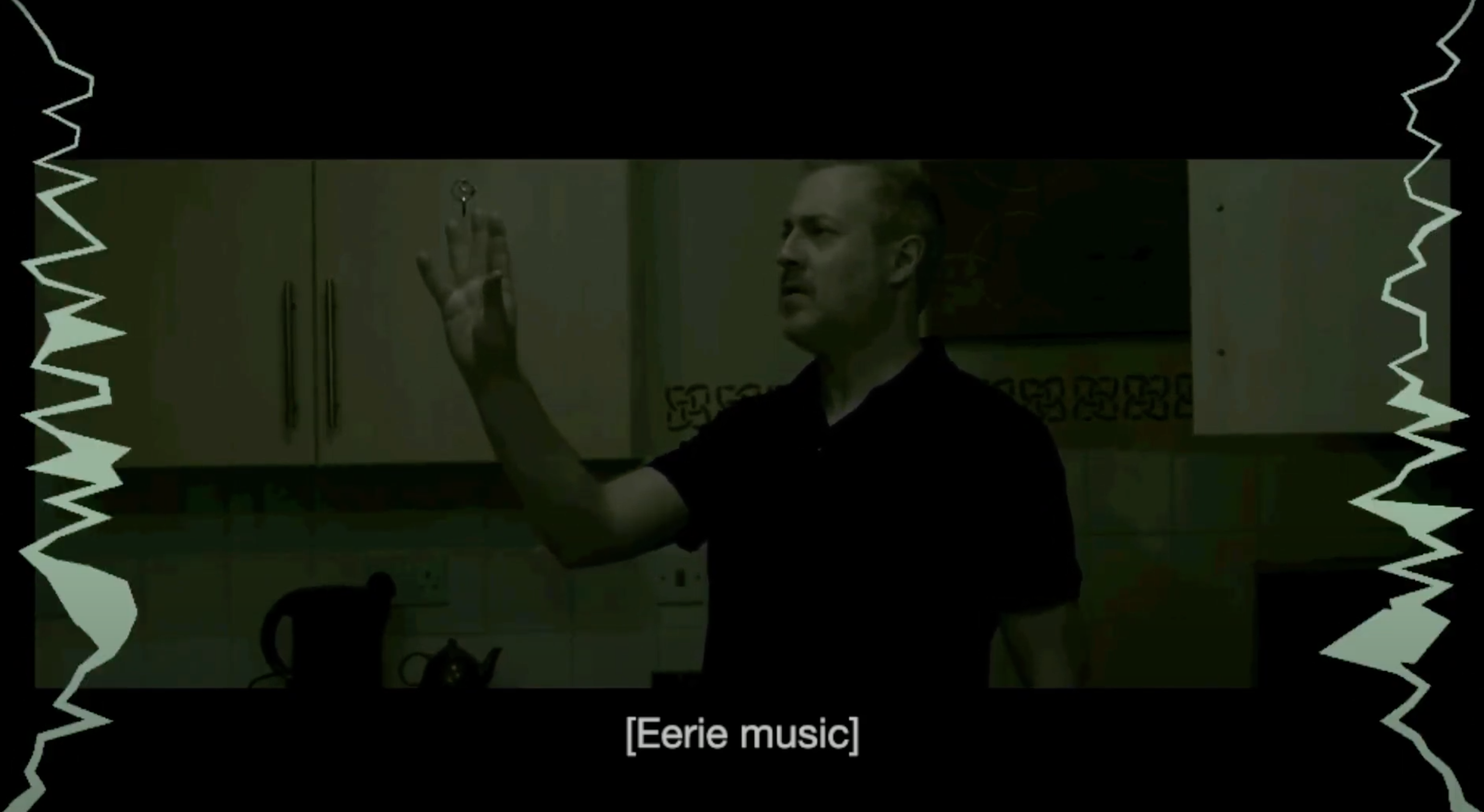 A dim-lit scene from a horror movie in which an man reaches for a mysterious key. Closed captioning reads: Eerie music with jagged green lines on the left and right.